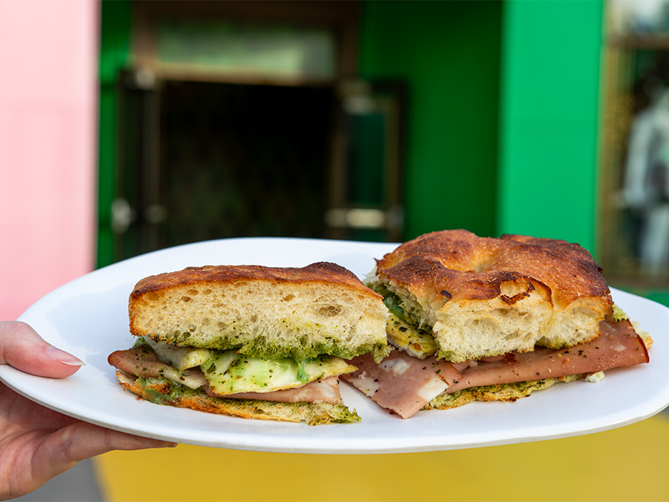 A hand holding a plate of the Emerald City Focaccia in front of Wicked: The Experience in Universal Studios Florida.