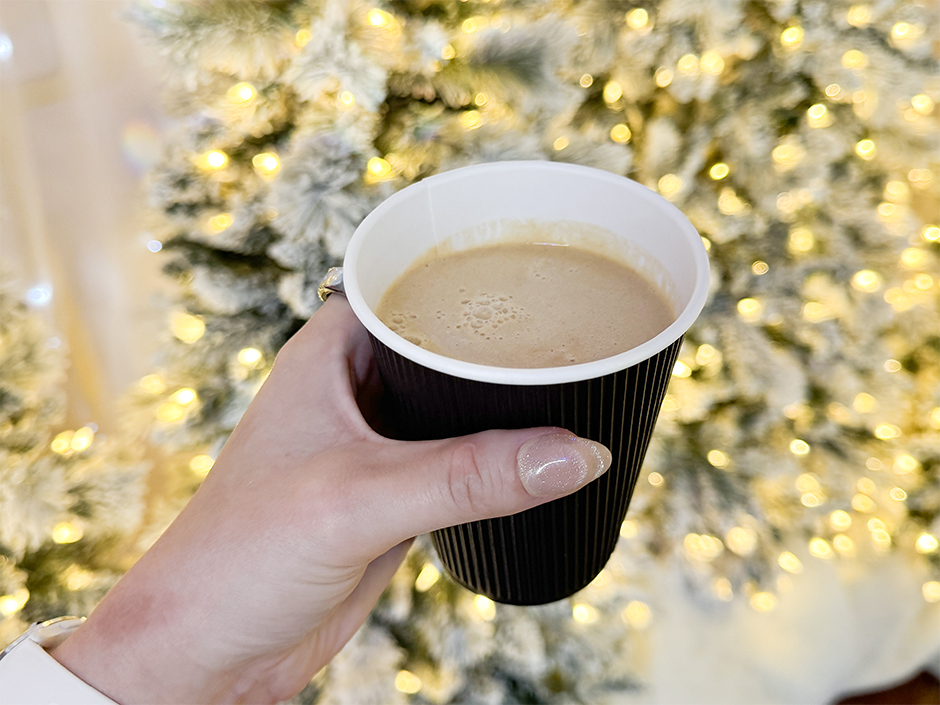 A hand holding the Hot Buttered Rum cocktail in front of Christmas lights